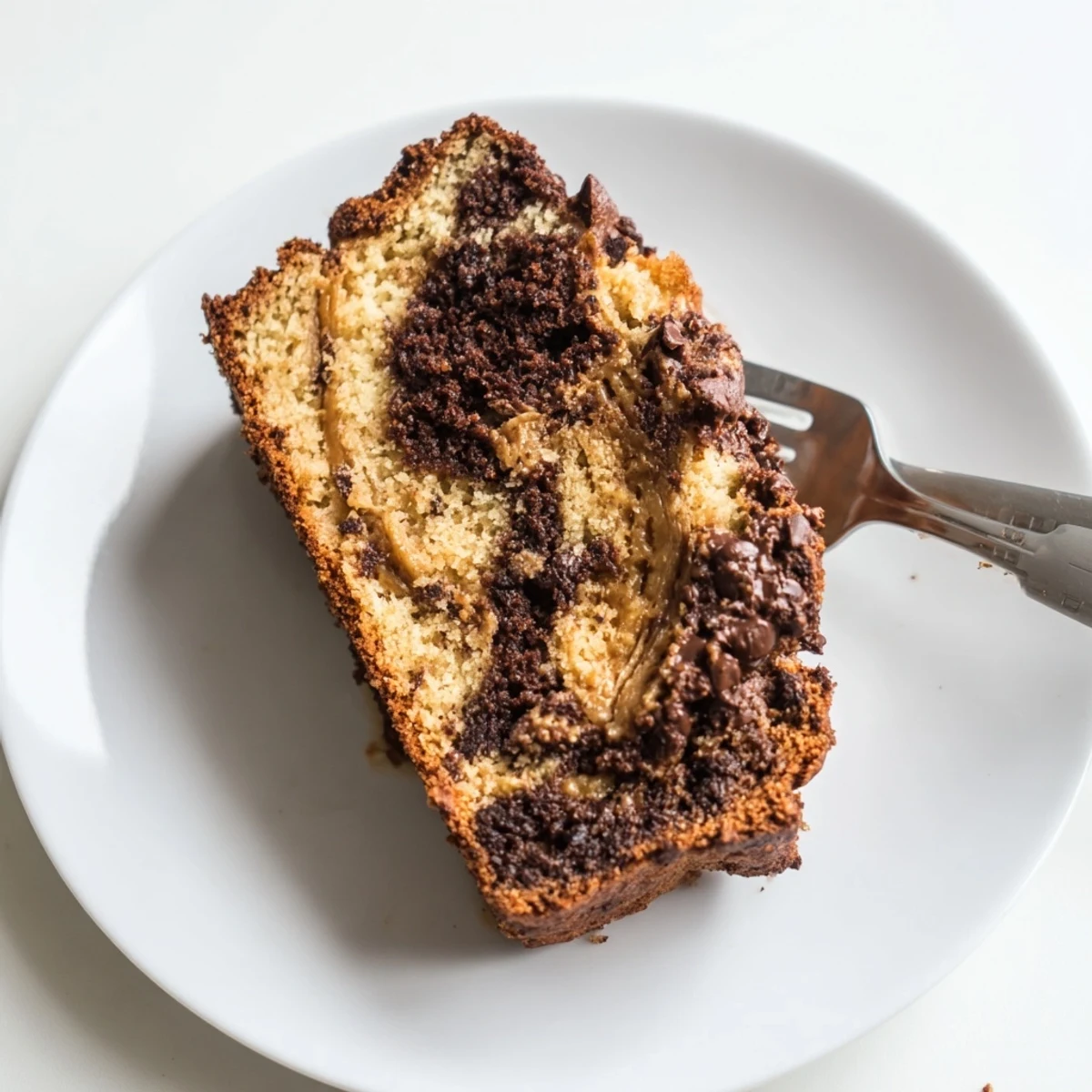 Moist chocolate peanut butter banana bread loaf sliced on a wooden board with coffee cup nearby
