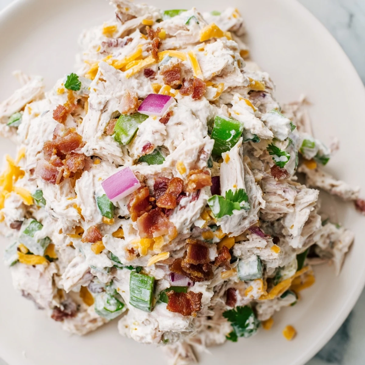 Creamy jalapeno popper keto chicken salad topped with crumbled bacon and fresh jalapeno slices in a white serving bowl