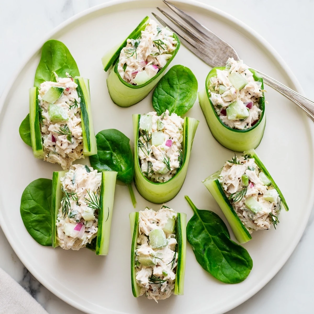 Close-up of chicken salad cucumber roll ups showcasing green spirals filled with herbed chicken mixture on white platter