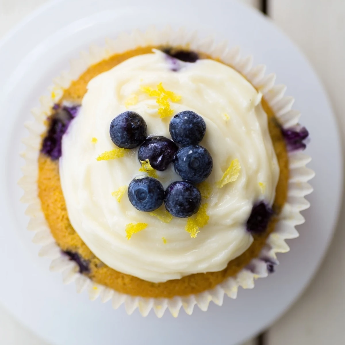 Golden baked lemon blueberry cupcakes with swirled cream cheese frosting on a white plate