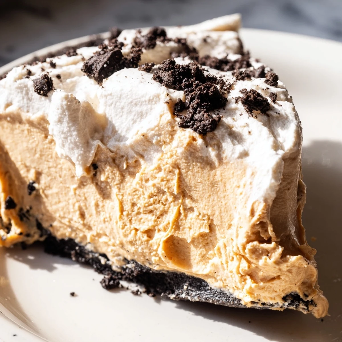 Creamy peanut butter Oreo pie sliced and topped with fluffy whipped cream and cookie crumbles