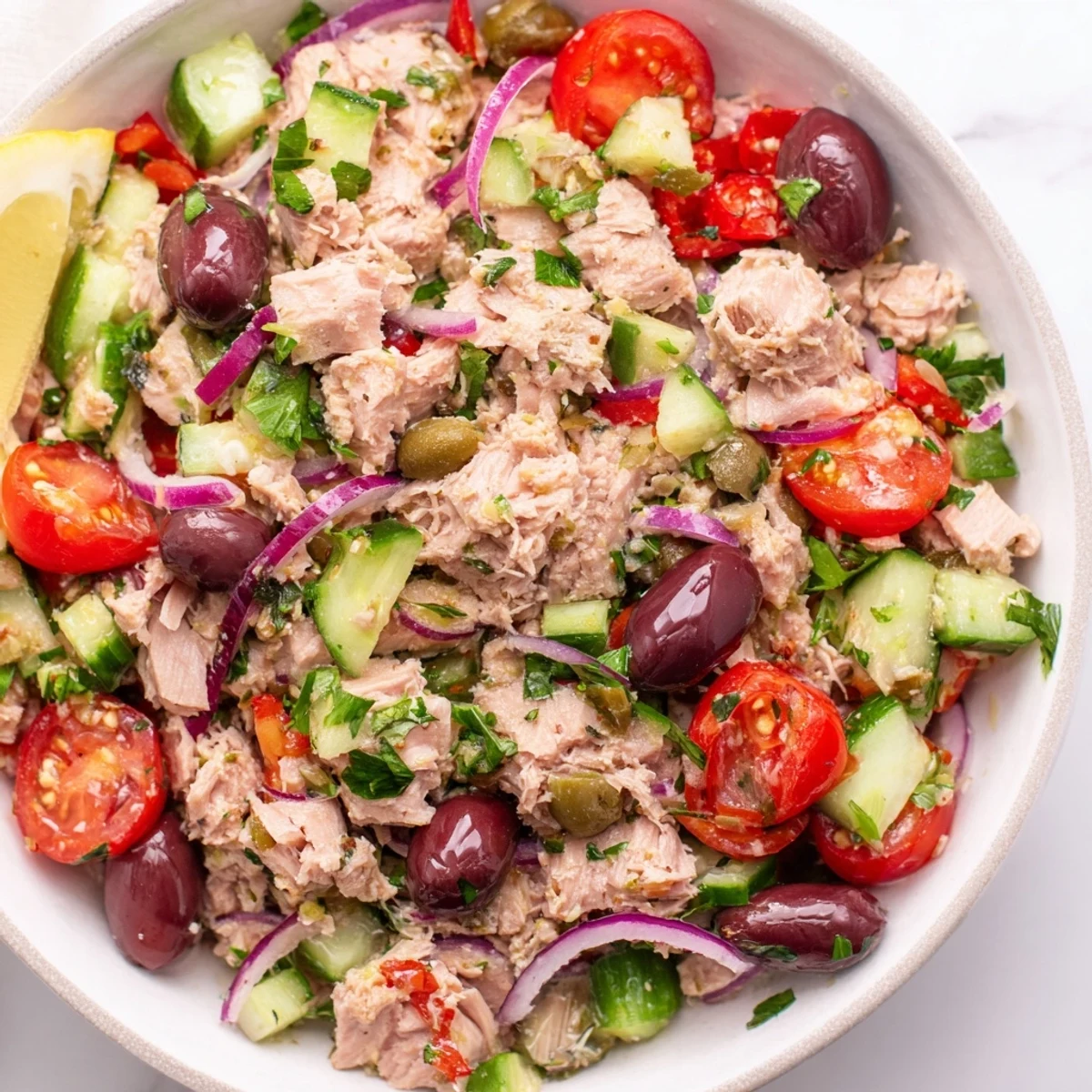 Mediterranean tuna salad in a white bowl with cherry tomatoes, olives, and fresh herbs