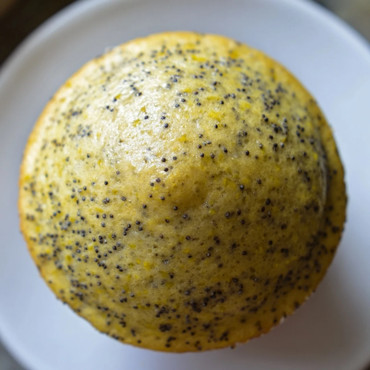 Moist lemon poppy seed muffins studded with tiny black seeds beside a bowl of fresh lemons