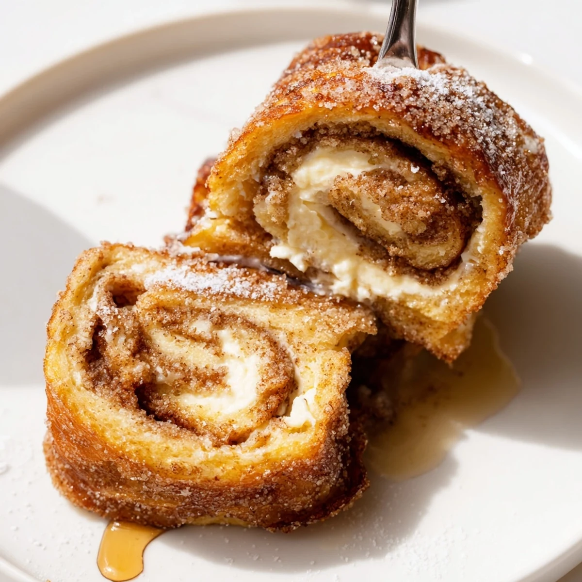 Skillet fried Cinnamon Roll French Toast Roll Ups served with maple syrup drizzle.