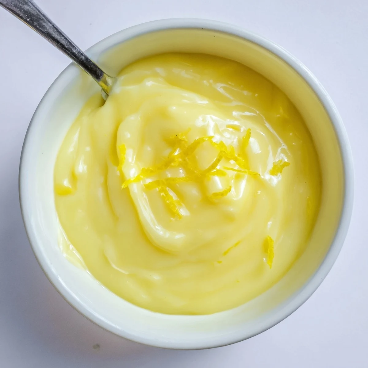 Silky, bright Lemon Curd Recipe cooling in sterilized jar beside whisk