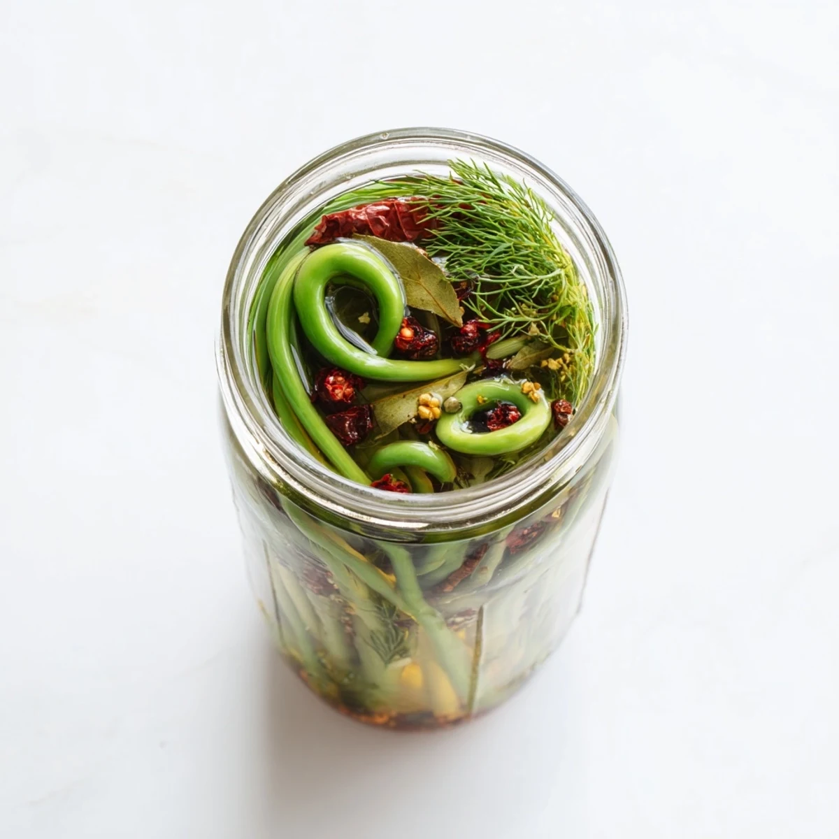 Crisp garlic scapes floating in clear brine with peppercorns mustard seeds and red pepper flakes visible
