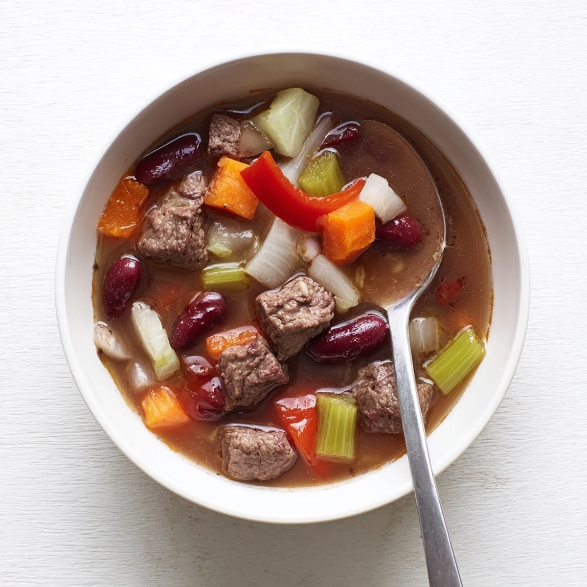 Hearty beef and bean soup delight simmered with smoked paprika and oregano, featuring chunks of beef, carrots, celery, and red bell pepper