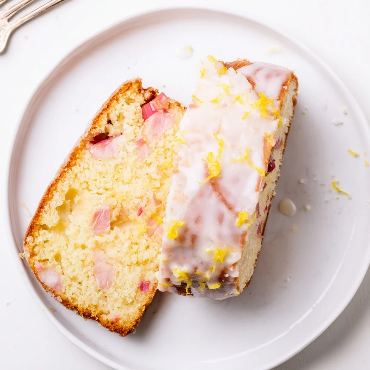 Golden rhubarb lemon drizzle cake with glistening icing and fresh red fruit pieces