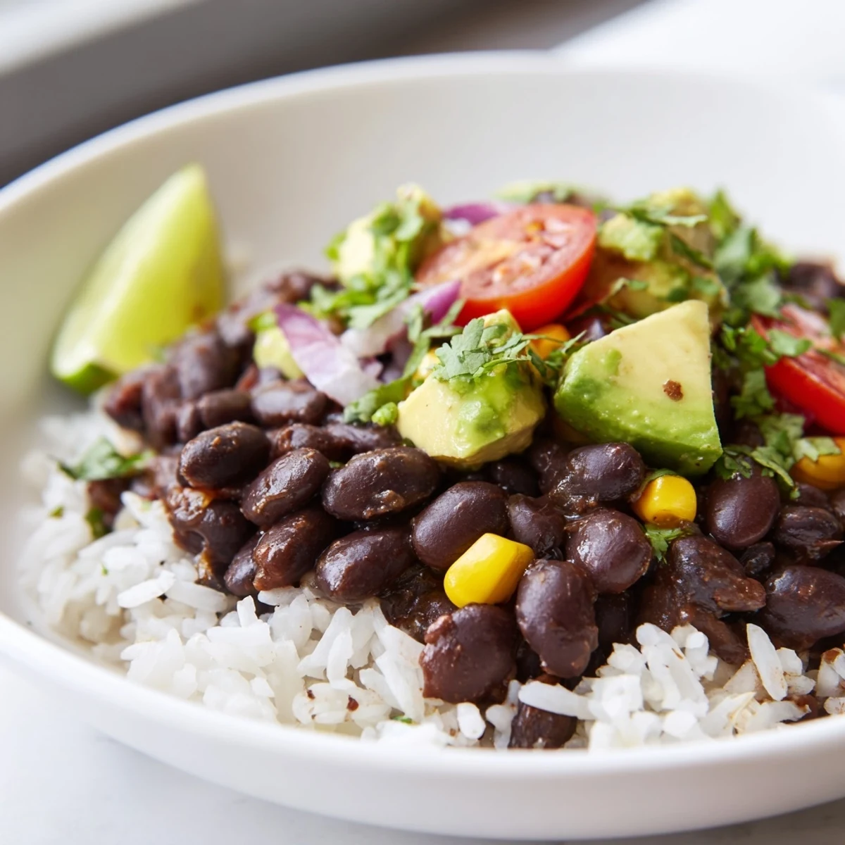Steaming black bean and rice bowl garnished with diced tomatoes and lime wedges
